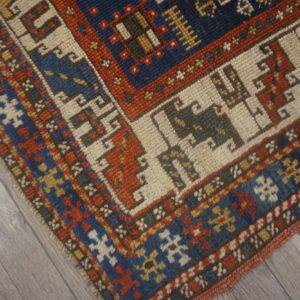 Detailed view of a geometric rug featuring navy, rust, and cream borders over gray wood flooring.