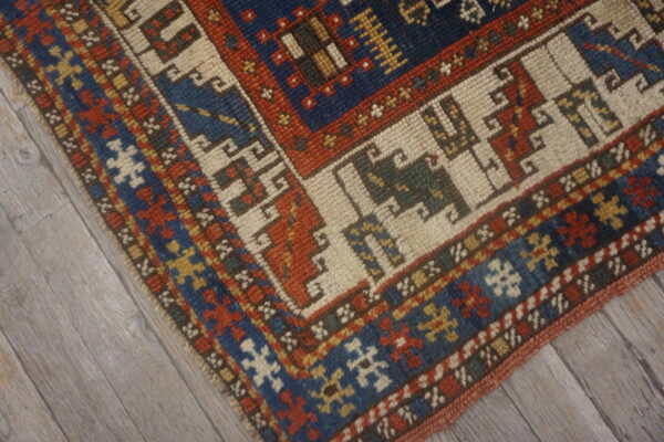 Detailed view of a geometric rug featuring navy, rust, and cream borders over gray wood flooring.