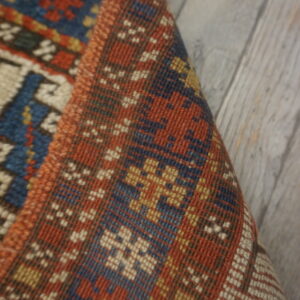 Close-up of a low-pile rug featuring a rust, blue, and gold geometric pattern on gray wood flooring.
