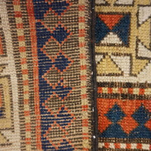 Close-up of a rug seam separating geometric patterns in rust, indigo, tan, and cream colors.