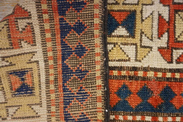Close-up of a rug seam separating geometric patterns in rust, indigo, tan, and cream colors.