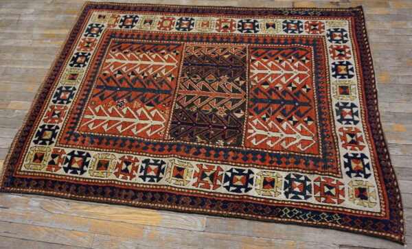 Tribal rug featuring geometric patterns in reddish-orange, navy, and cream on gray wood flooring.