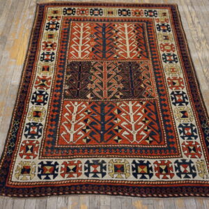 Geometric low-pile rug in rust, navy, and cream with stylized tree motifs on distressed wood.