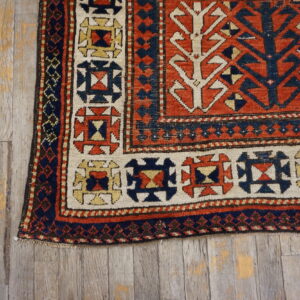 Geometric rust, navy, and cream low-pile rug corner rests on weathered wood planks.