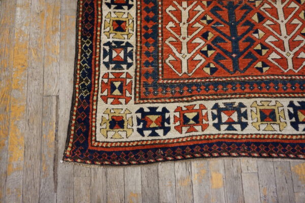 Geometric rust, navy, and cream low-pile rug corner rests on weathered wood planks.