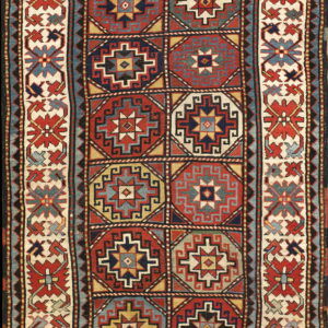 Low-pile geometric rug featuring red and blue octagonal medallions surrounded by a patterned ivory border.