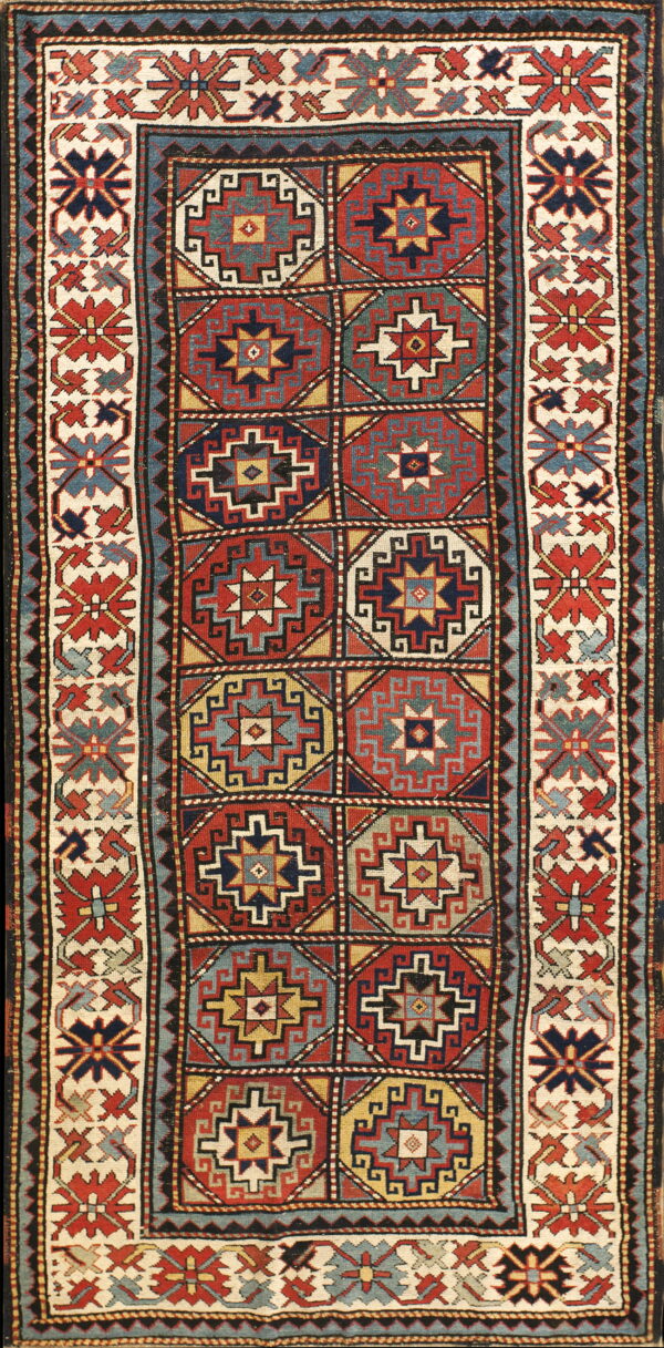 Low-pile geometric rug featuring red and blue octagonal medallions surrounded by a patterned ivory border.