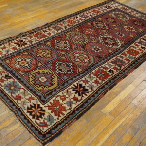 Geometric diamond-lattice rug in red, blue, and cream colors rests on light-toned hardwood planks.