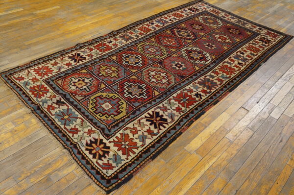 Geometric diamond-lattice rug in red, blue, and cream colors rests on light-toned hardwood planks.