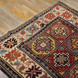 Low-pile rug with a geometric red, blue, cream, and yellow pattern rests on light wood planks.
