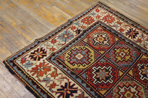 Low-pile rug with a geometric red, blue, cream, and yellow pattern rests on light wood planks.