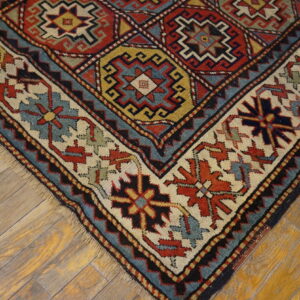 Low-pile rug corner showing red, cream, blue, and yellow geometric patterns on weathered wood planks.