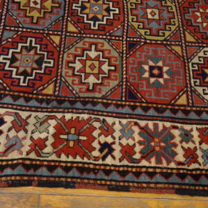 Geometric rug detail in red, blue, and gold with a patterned field and thick border on wood floor.