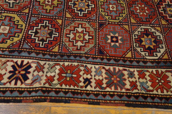 Geometric rug detail in red, blue, and gold with a patterned field and thick border on wood floor.