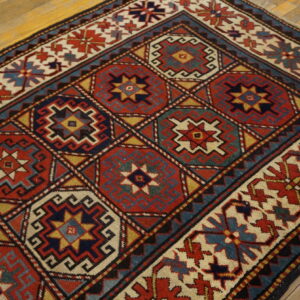 Red, navy, teal, and gold low-pile rug with repeating geometric medallions rests on natural wood floorboards.