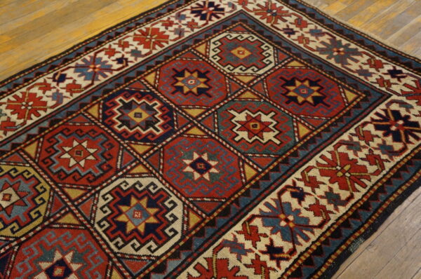 Red, navy, teal, and gold low-pile rug with repeating geometric medallions rests on natural wood floorboards.