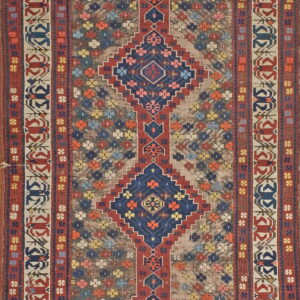 Low-pile rug with a long vertical axis of red and navy geometric diamonds on a multi-colored background field.