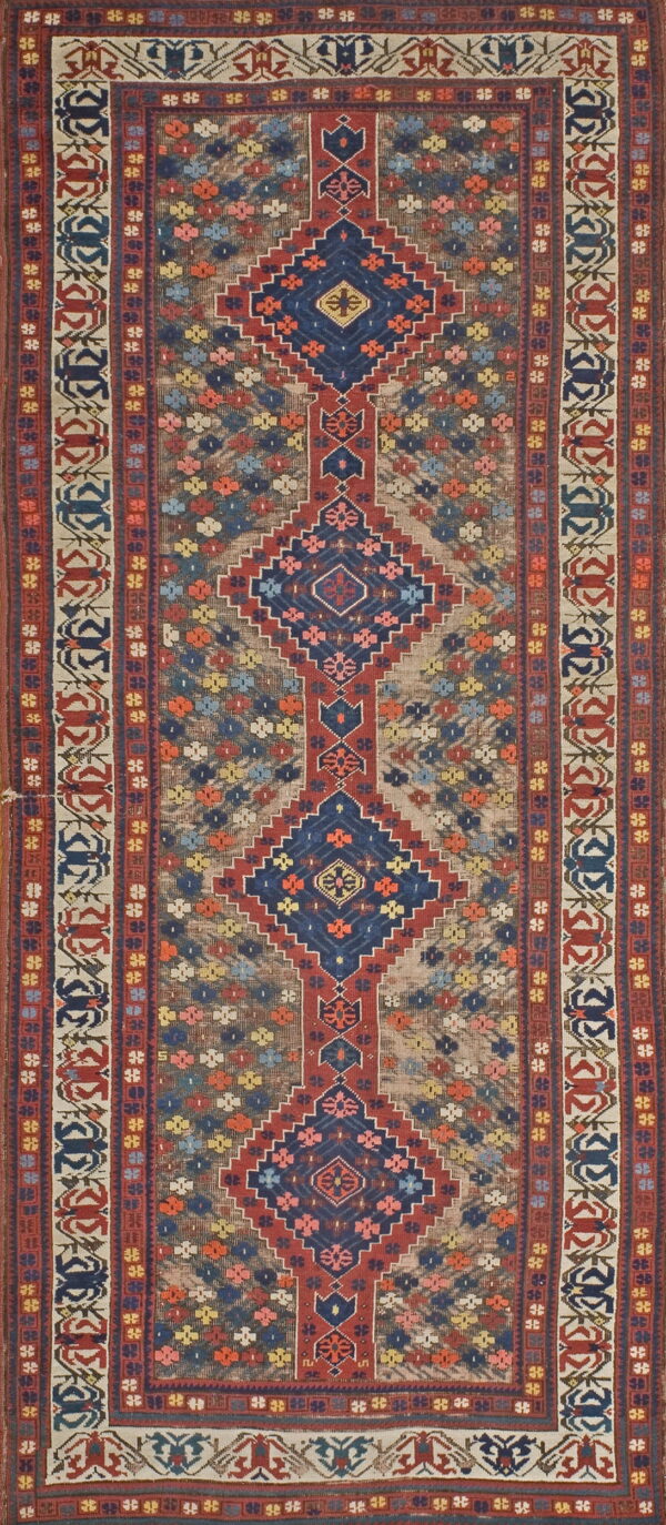 Low-pile rug with a long vertical axis of red and navy geometric diamonds on a multi-colored background field.