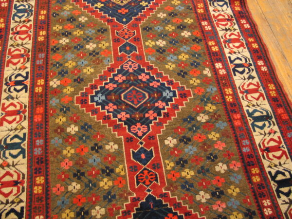 Low-pile rug with red, navy, and brown geometric patterns and floral accents resting on a wood floor.