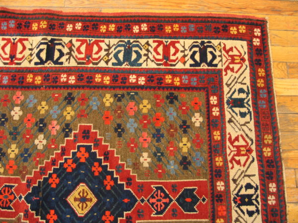 Detailed corner of a low-pile rug in red, navy, and olive geometric patterns, sitting on hardwood floor planks.