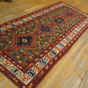 Geometric blue and red runner rug with a multi-colored floral field, displayed on a worn wood plank floor.