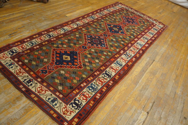 Geometric blue and red runner rug with a multi-colored floral field, displayed on a worn wood plank floor.