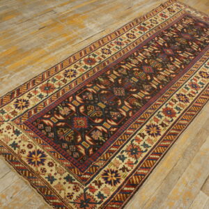 Dark geometric runner rug with cream and red borders rests on distressed, light-colored hardwood flooring.