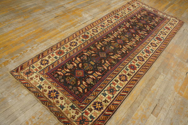 Dark geometric runner rug with cream and red borders rests on distressed, light-colored hardwood flooring.