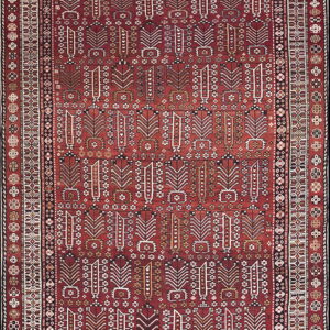 A vertically oriented rug with a dark red field and repeating ivory geometric motifs surrounded by patterned borders.
