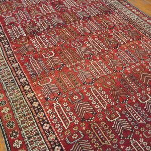 A deep red rug featuring stylized white, black, and beige vertical patterns in the field over wood plank flooring.