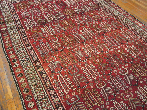 A deep red rug featuring stylized white, black, and beige vertical patterns in the field over wood plank flooring.