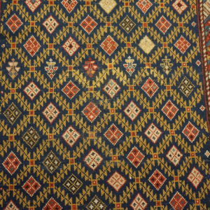 Detailed view of a low-pile rug featuring a navy field, gold motifs, red diamonds, and striped geometric borders.