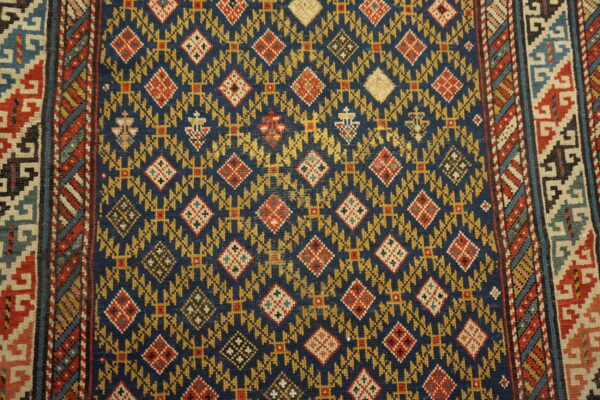 Detailed view of a low-pile rug featuring a navy field, gold motifs, red diamonds, and striped geometric borders.