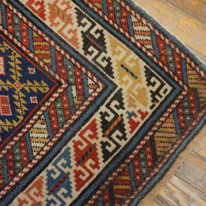 Low-pile rug with geometric blue, red, and yellow patterns rests on rustic wooden planks.