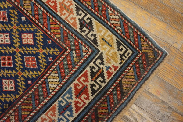 Low-pile rug with geometric blue, red, and yellow patterns rests on rustic wooden planks.
