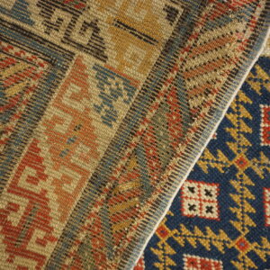 Folded rug detail showing a dark blue geometric pile next to a flatwoven band of red, yellow, and tan patterns.