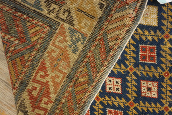 Folded rug detail showing a dark blue geometric pile next to a flatwoven band of red, yellow, and tan patterns.