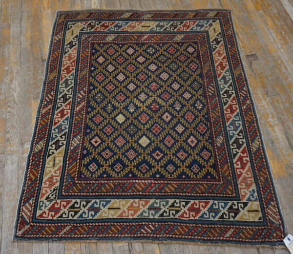 Navy, red, and gold geometric rug with intricate borders lying on distressed wood floorboards.