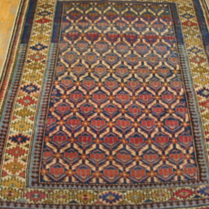 Geometric blue and red patterned rug with multiple borders rests on light-toned wooden floor planks.