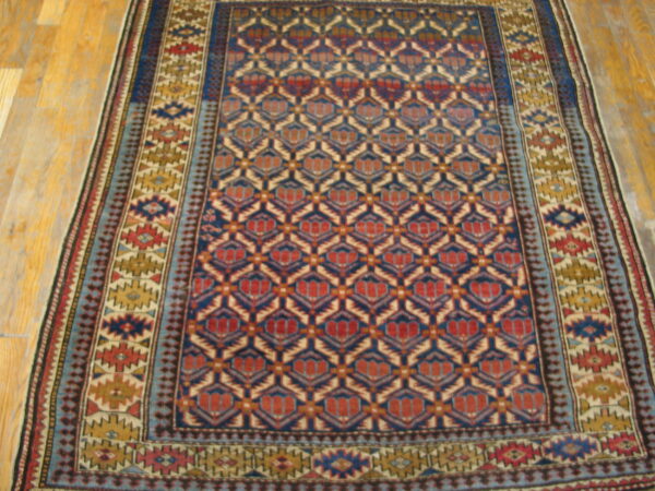 Geometric blue and red patterned rug with multiple borders rests on light-toned wooden floor planks.