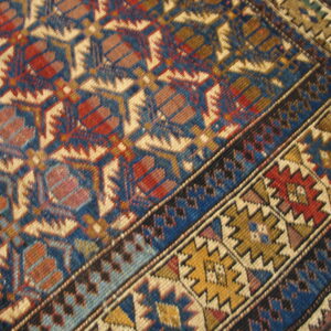 Geometric rug with repeating hexagonal motifs and complex borders in navy, rust, gold, and tan colors.