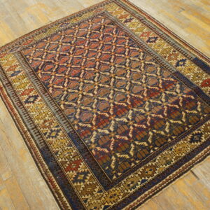 Low-pile rug with repeating geometric patterns in blue, rust, and yellow on distressed wood flooring.