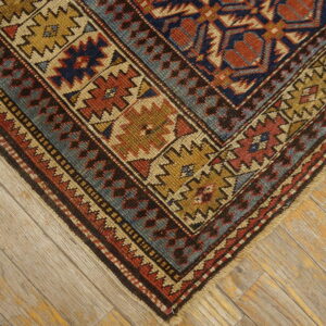 Red, navy, and gold geometric rug border corner resting on distressed blonde wood flooring.
