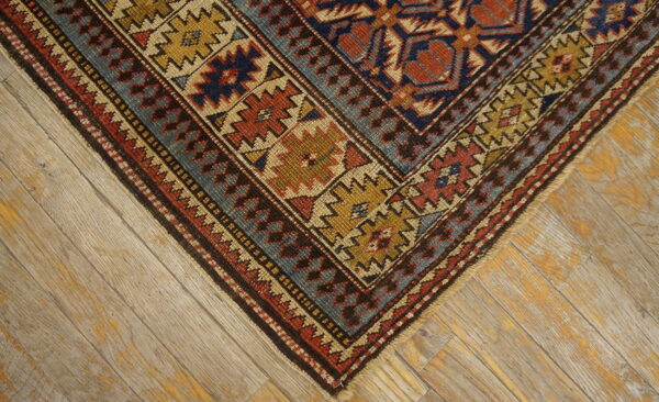 Red, navy, and gold geometric rug border corner resting on distressed blonde wood flooring.