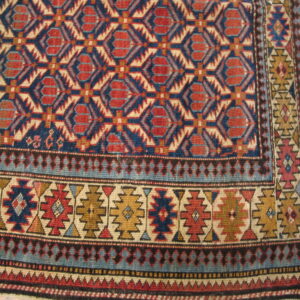Detailed view of a low-pile geometric rug in red, navy, beige, and gold on wood flooring.