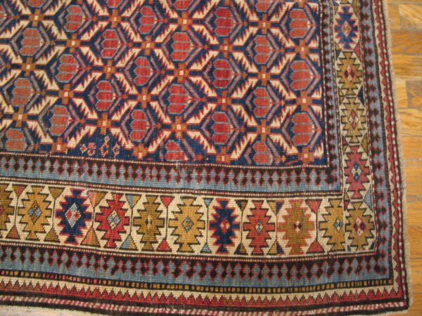 Detailed view of a low-pile geometric rug in red, navy, beige, and gold on wood flooring.