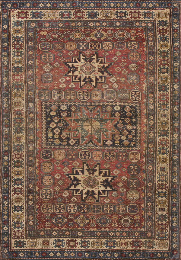 Faded red rug with complex geometric designs, featuring a large dark blue central panel and multi-layered border.
