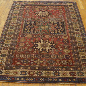 Red and navy geometric patterned rug with central stars laid on glossy wooden floorboards.