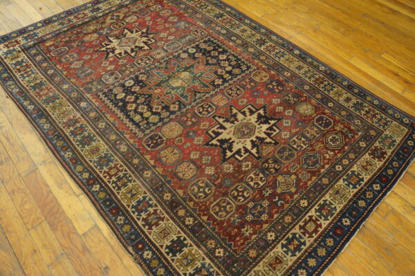 Red and navy geometric rug with intricate tribal motifs rests on light brown hardwood flooring.