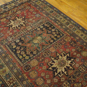 Distressed red and blue tribal rug featuring complex geometric medallions rests on light wood plank flooring.